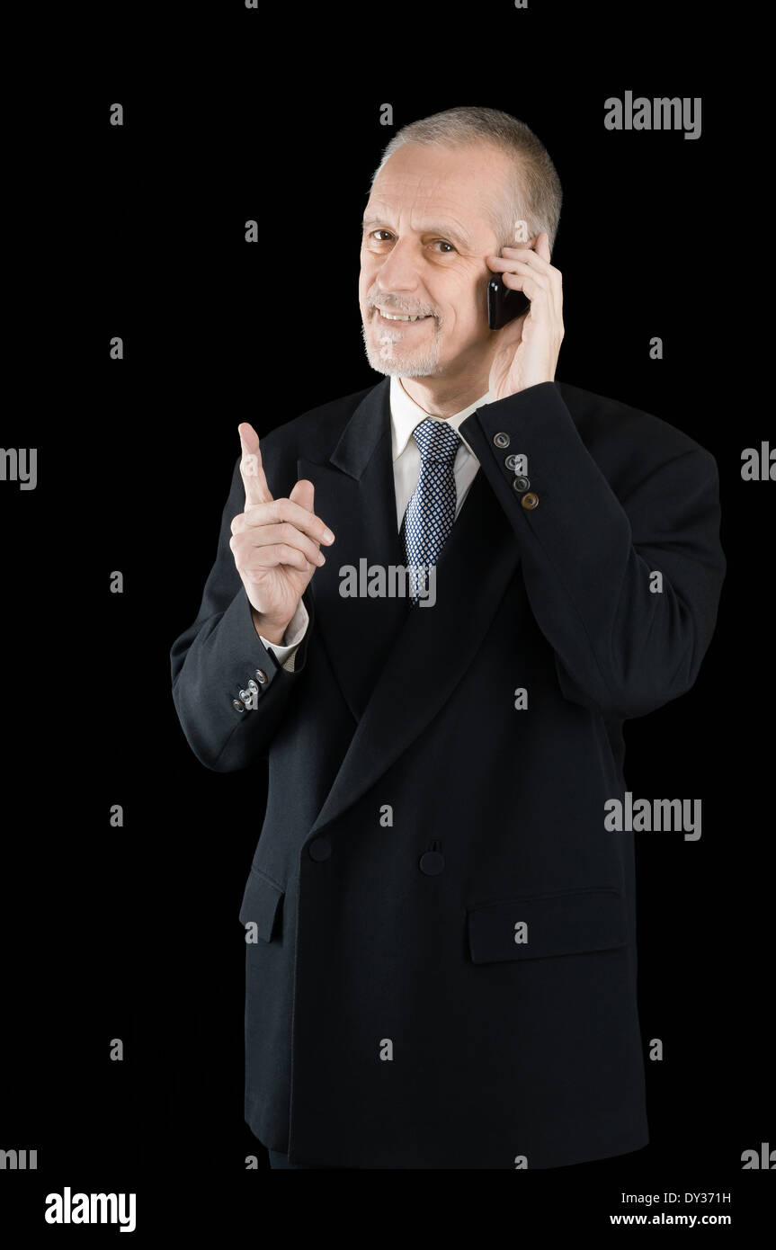 Un gradevole imprenditore indossando un abito nero di sorridere mentre si parla al telefono cellulare, su sfondo nero Foto Stock