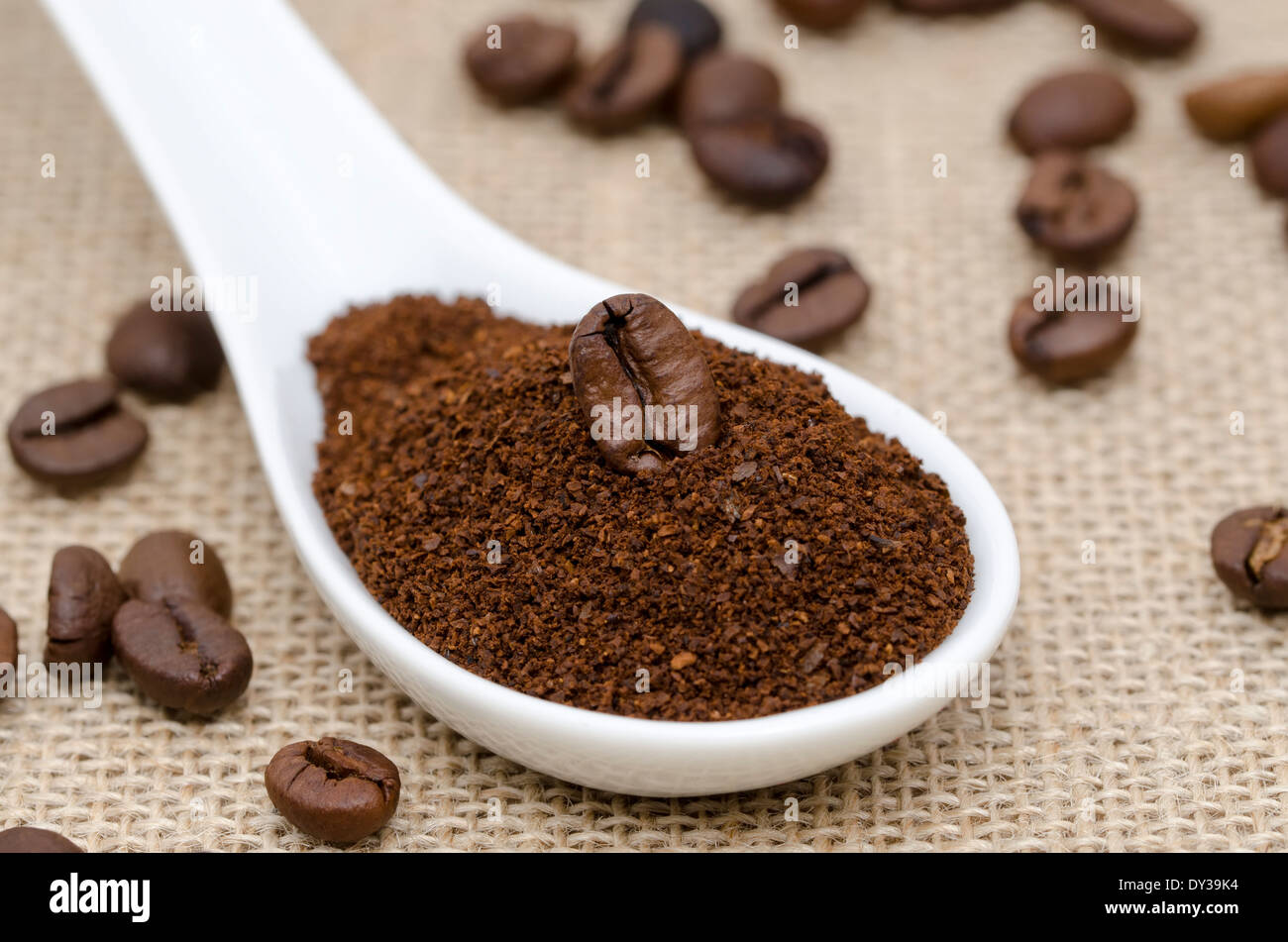 Porcellana Bianca cucchiaio con il caffè macinato e i chicchi di caffè su una tela ruvida Foto Stock