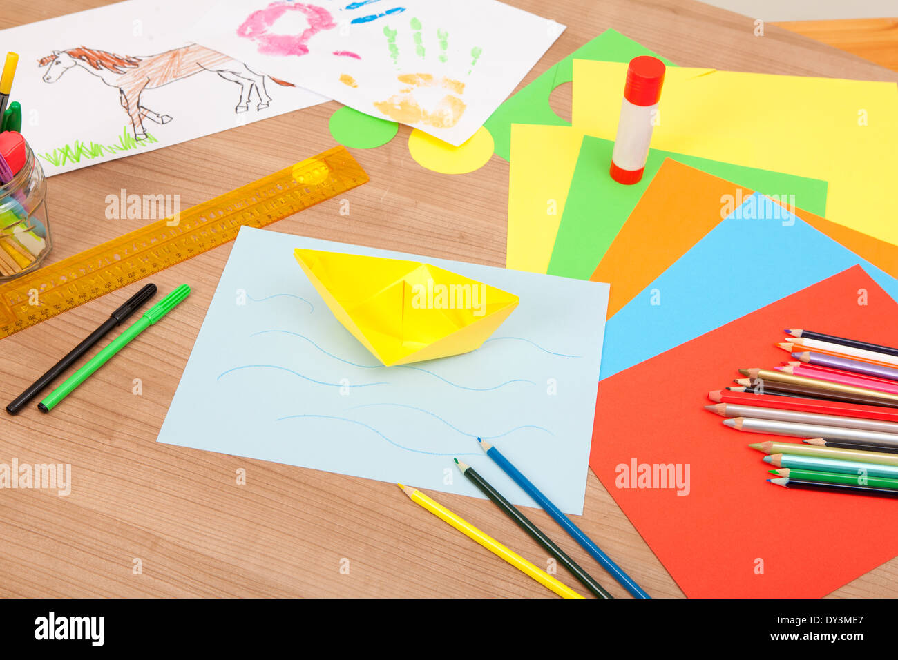 Carta colorata giacente su di un piano per la piegatura di oggetti, in background dei bambini immagini dipinte Foto Stock