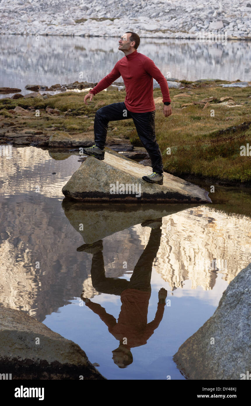 Outdoorsman intensificazione su una roccia su un Sierra lake shore con la riflessione Foto Stock
