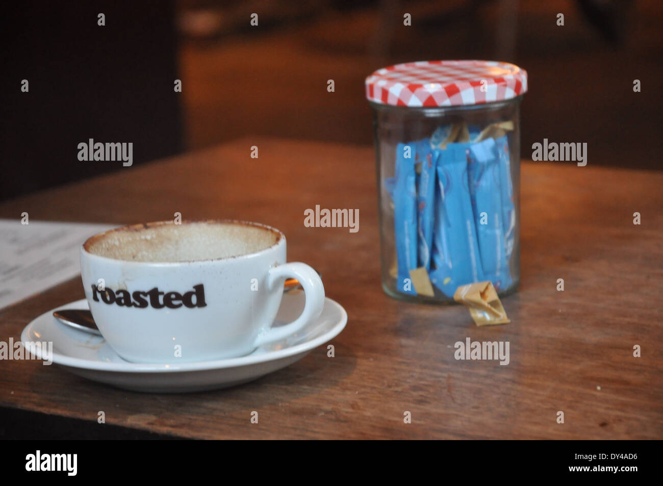 Un vuoto che la tazza di caffè contrassegnati '' arrosto e jar di porzioni di zucchero su una tavola di legno Foto Stock
