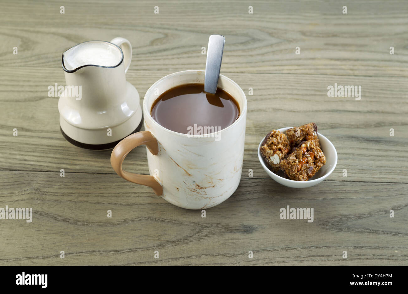 Closeup foto orizzontale di una tazza piena di caffè, spuntini e crema nel beccuccio versatore con legno invecchiato sotto Foto Stock