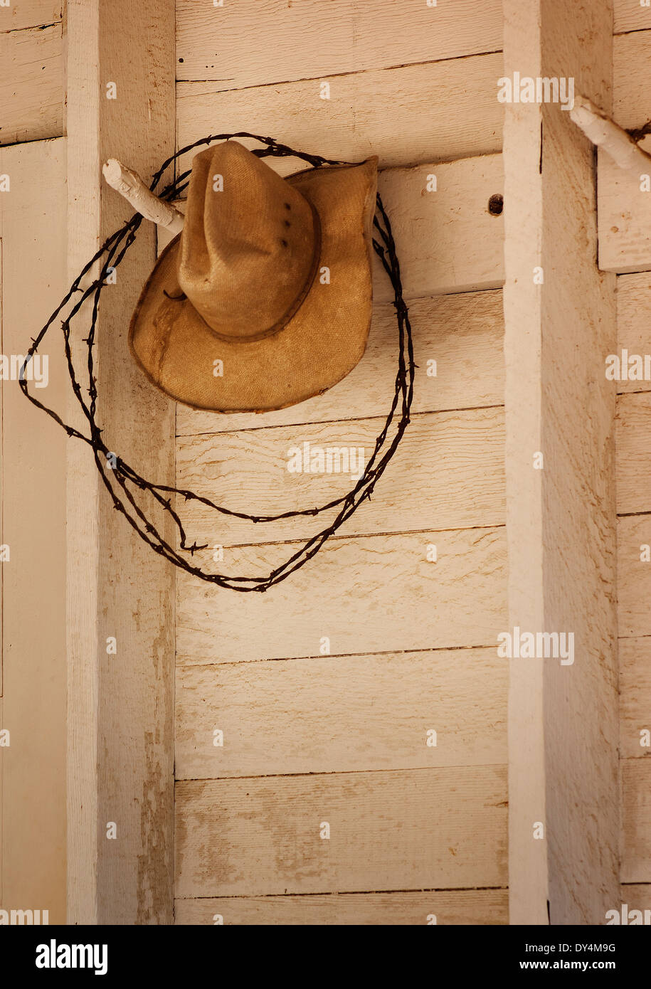 Un vecchio cappello da cowboy appesi a un picchetto in legno con filo spinato su un bianco al di fuori del muro del granaio Foto Stock