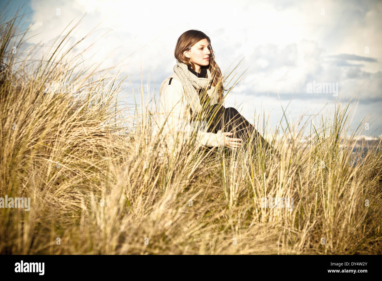Giovane donna seduta in dune di sabbia, Bournemouth Dorset, Regno Unito Foto Stock