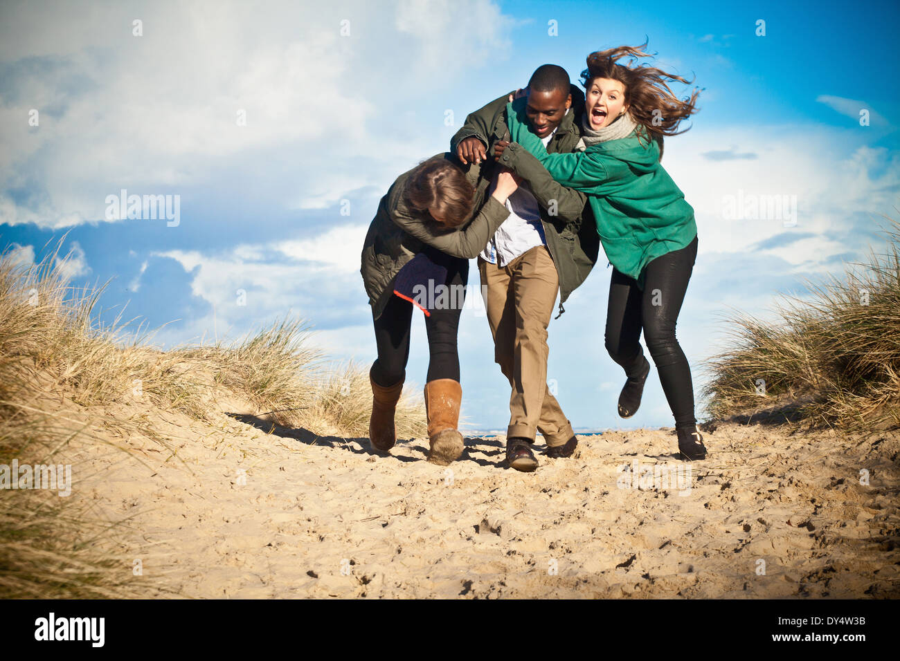Giovani amici adulti in esecuzione in dune di sabbia, Bournemouth Dorset, Regno Unito Foto Stock