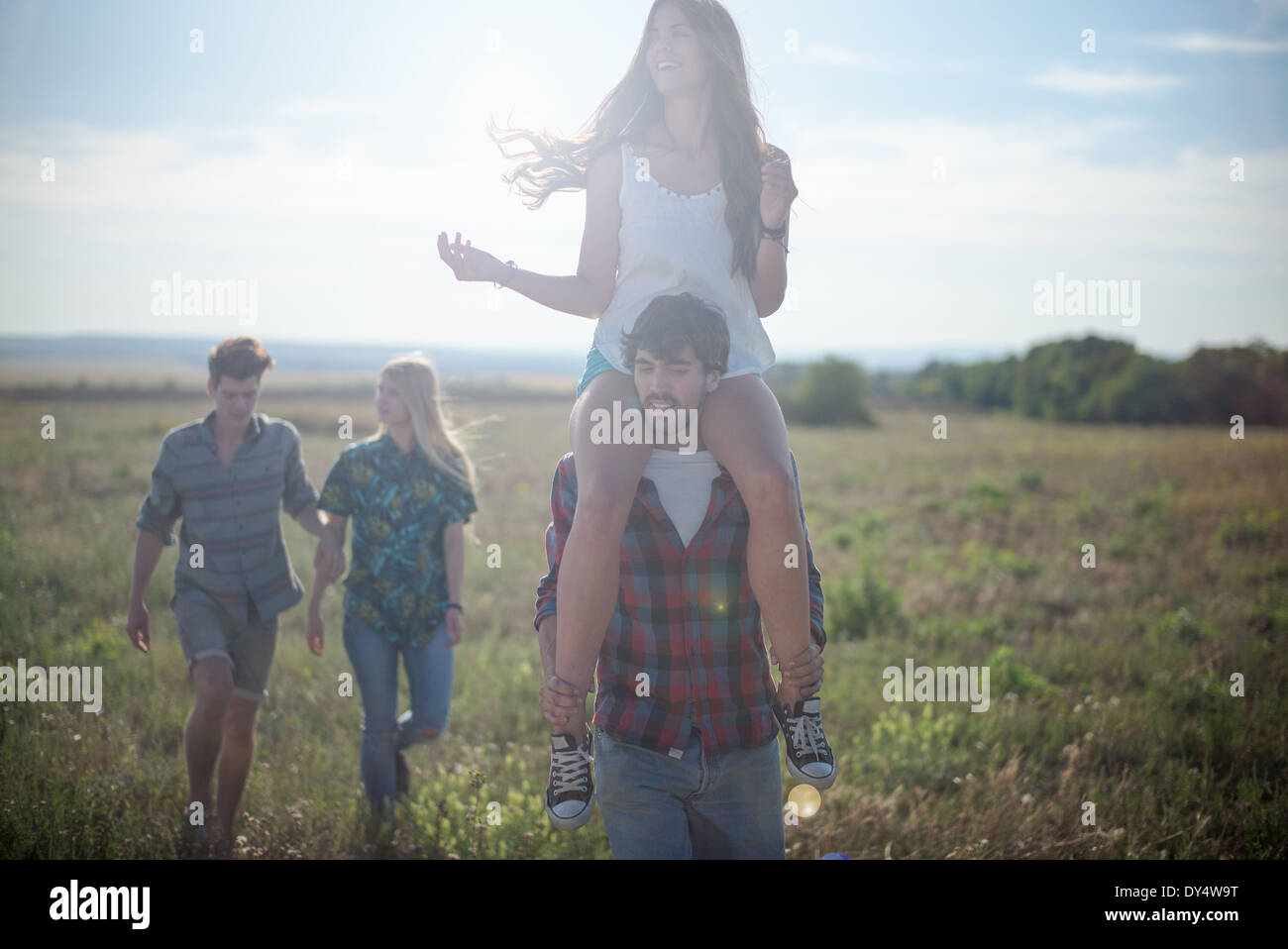 Gli amici passeggiando nel campo, uomo donna che porta sulle spalle Foto Stock