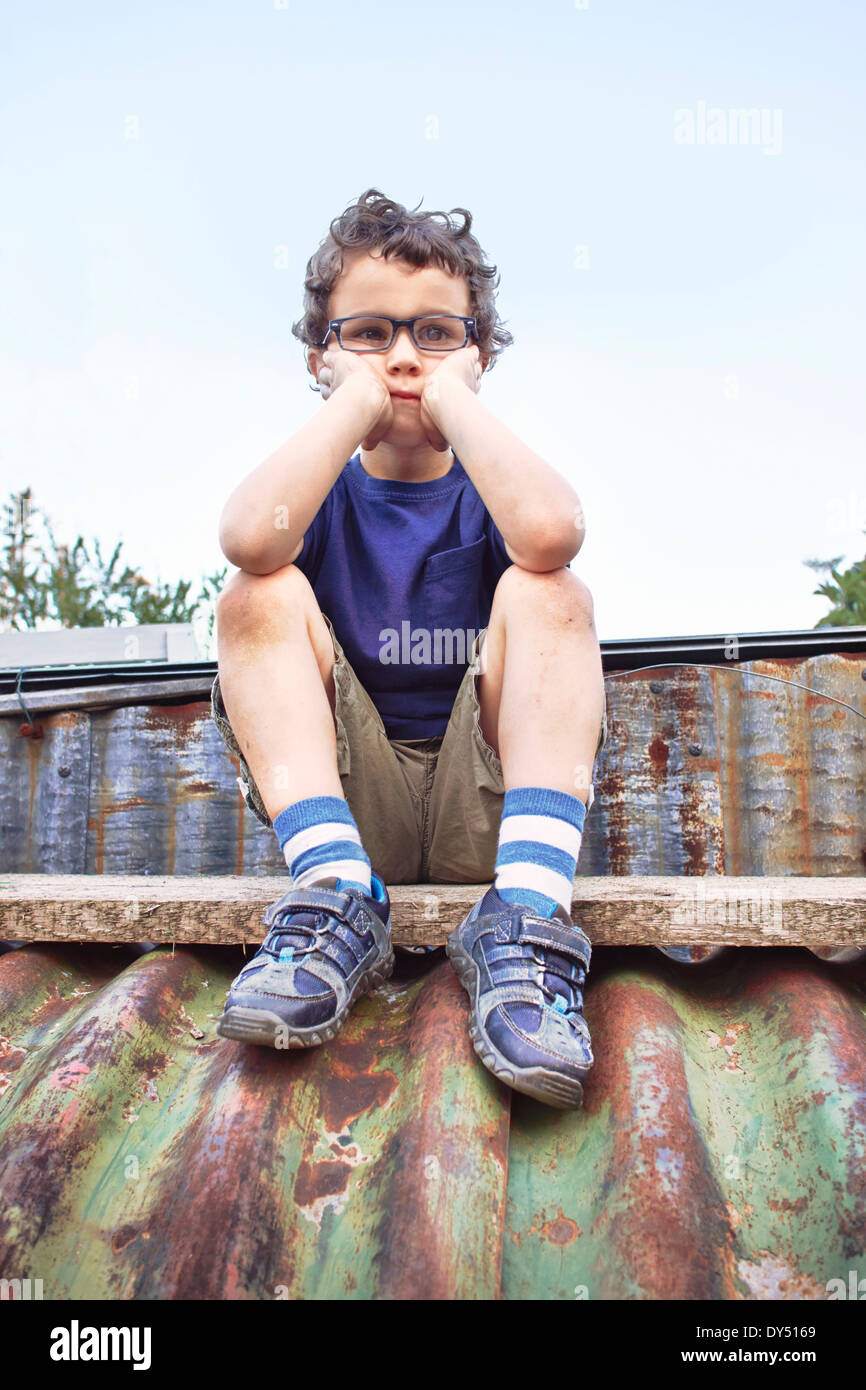 Glum piccolo ragazzo seduto sul tetto Foto Stock
