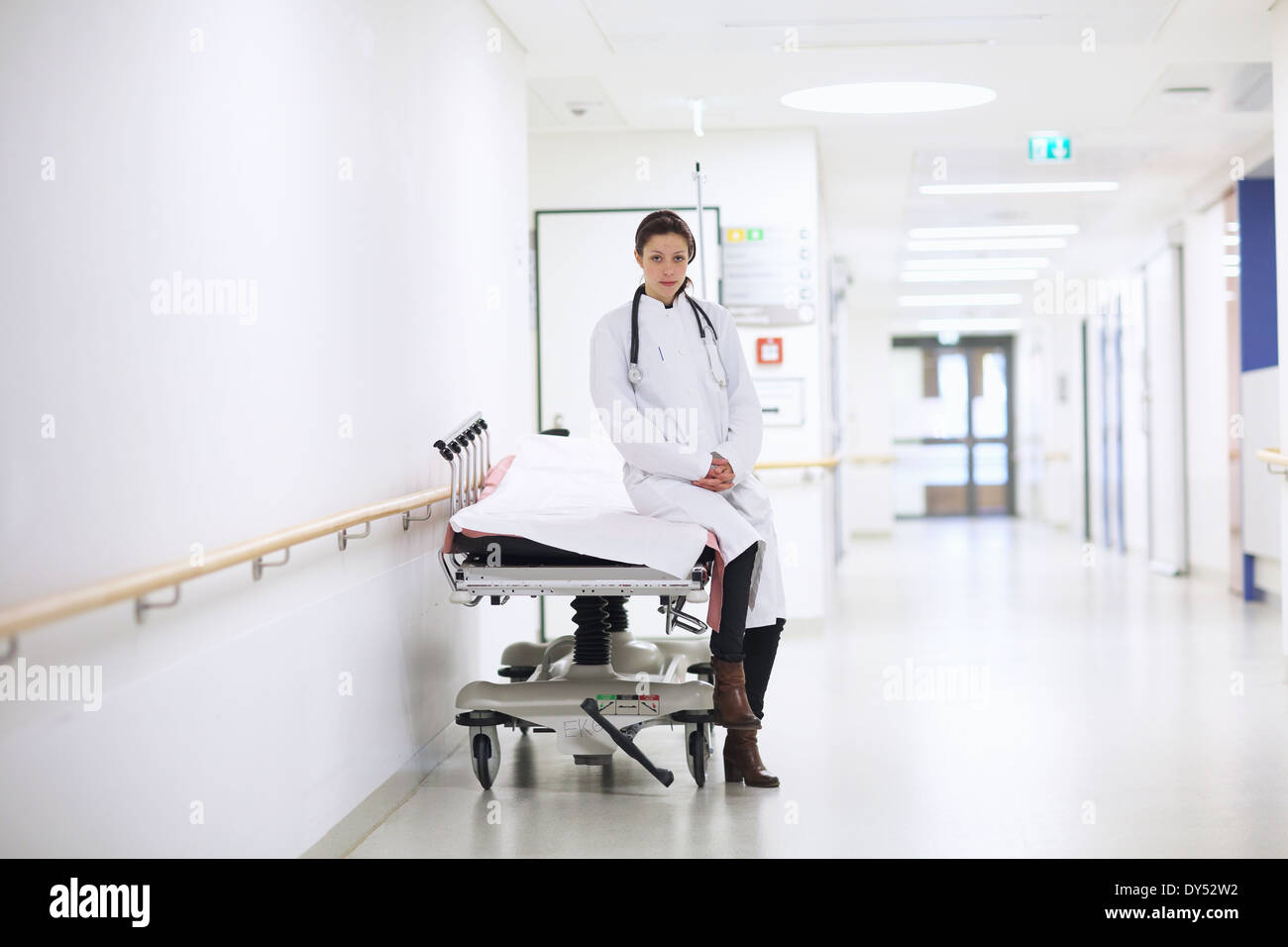 Ritratto di medico donna seduta sul carrello in ospedale in corridoio Foto Stock