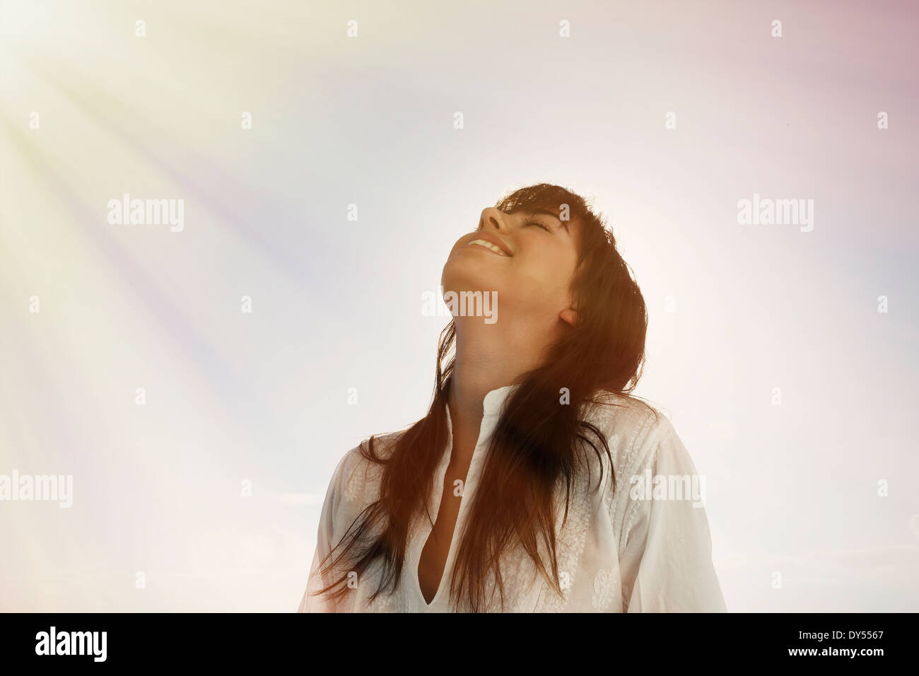 Giovane donna guardando in alto, raggi di sole sulla faccia Foto Stock