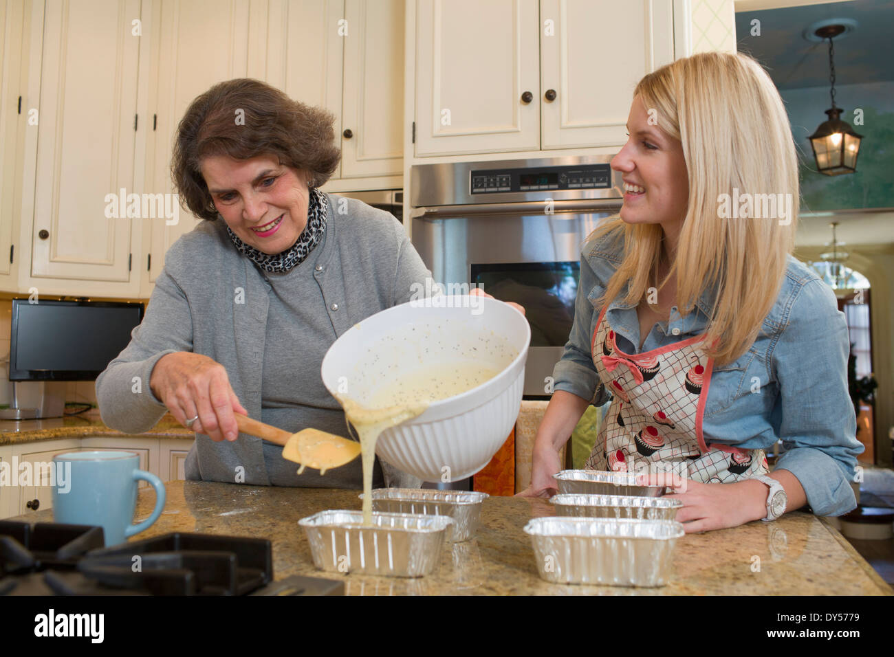 Donna Senior e nipote versando la miscela in teglie Foto Stock