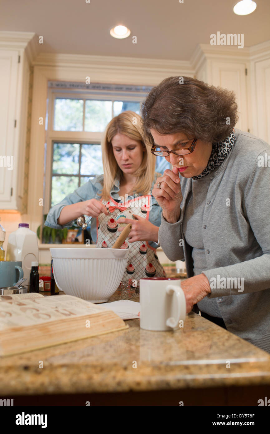 Donna Senior e nipote versando la cottura in cucina Foto Stock