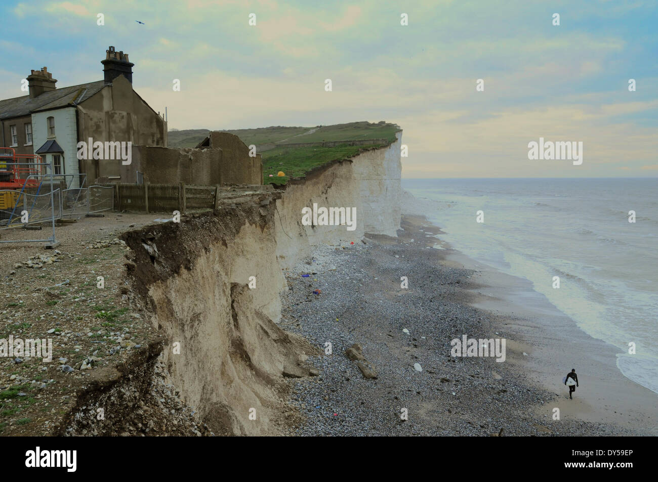 Birling Gap, East Sussex, Regno Unito..7 Aprile 2014..resti di cottage no3 appollaiato sul ciglio della scogliera. Le frane continuano. Surfer cammina indietro lungo la spiaggia, in basso a destra, dopo approfittando delle onde.David Burr/Alamy Live News Foto Stock