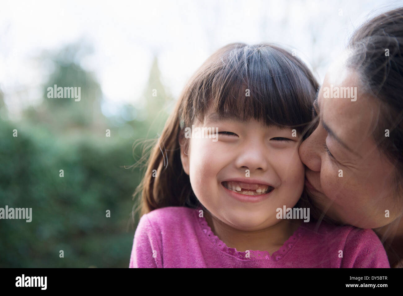 Ragazza baciato sulla guancia da sua madre in giardino Foto Stock