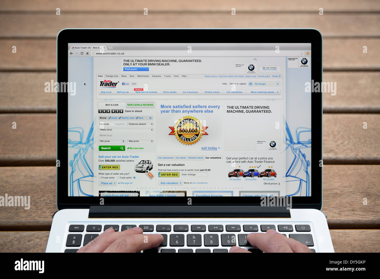 L'Auto Trader del sito su MacBook contro una panca in legno sfondo all'aperto tra cui un uomo le dita (solo uso editoriale). Foto Stock