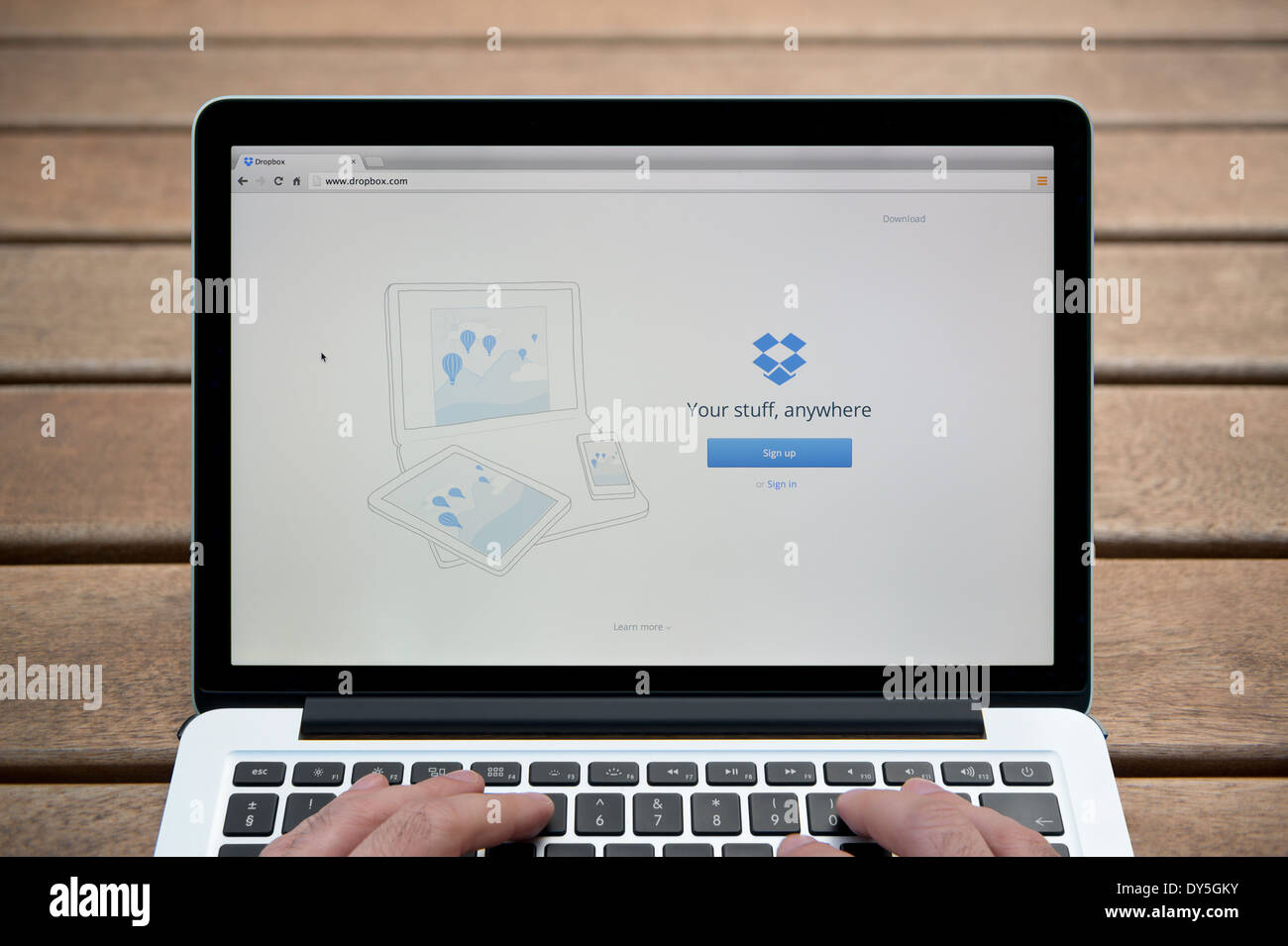 Il sito web di Dropbox sul MacBook contro una panca in legno sfondo all'aperto tra cui un uomo le dita (solo uso editoriale). Foto Stock