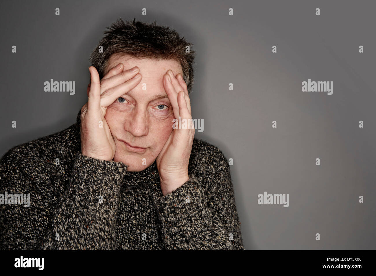 Un uomo un po' stressato con la testa nelle mani che guarda la macchina fotografica Foto Stock