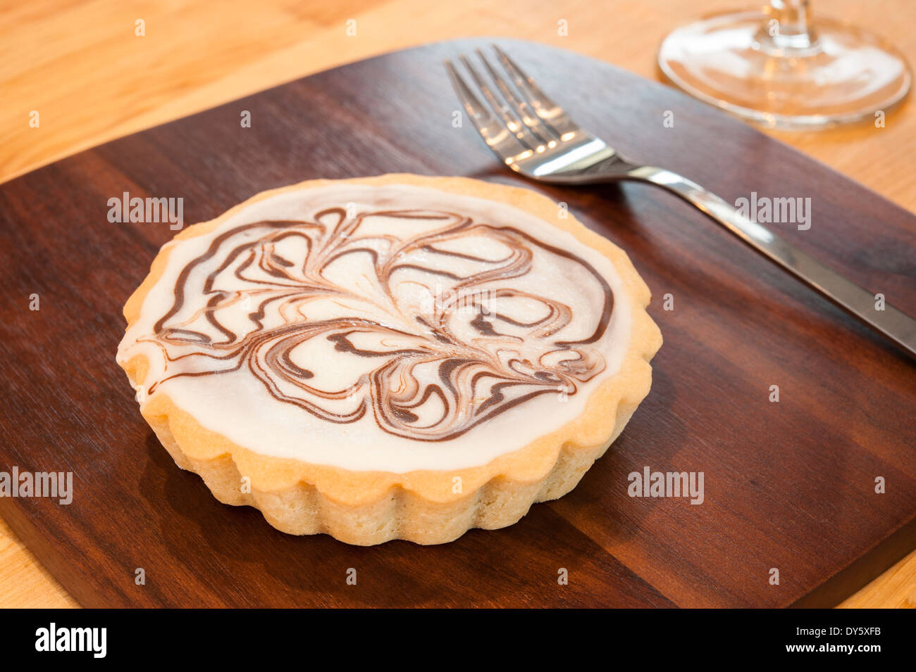 Il cioccolato bianco crostata con cioccolato fondente volute sul piatto di legno Foto Stock