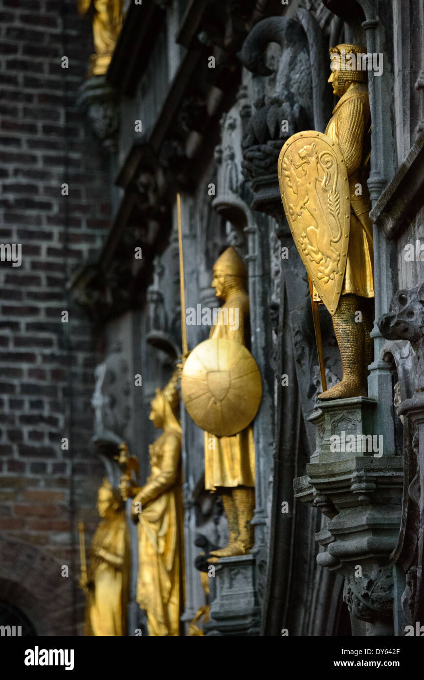 BRUGES, Belgio: Statue dorate adornano l'esterno della Basilica del Santo sangue, una chiesa medievale in Piazza Burg. La struttura gotica ornata, famosa per ospitare una reliquia del sangue di Cristo, presenta elaborate decorazioni architettoniche che includono queste figure dorate. Questi elementi scultorei dimostrano le ricche tradizioni artistiche dell'architettura religiosa medievale. Foto Stock