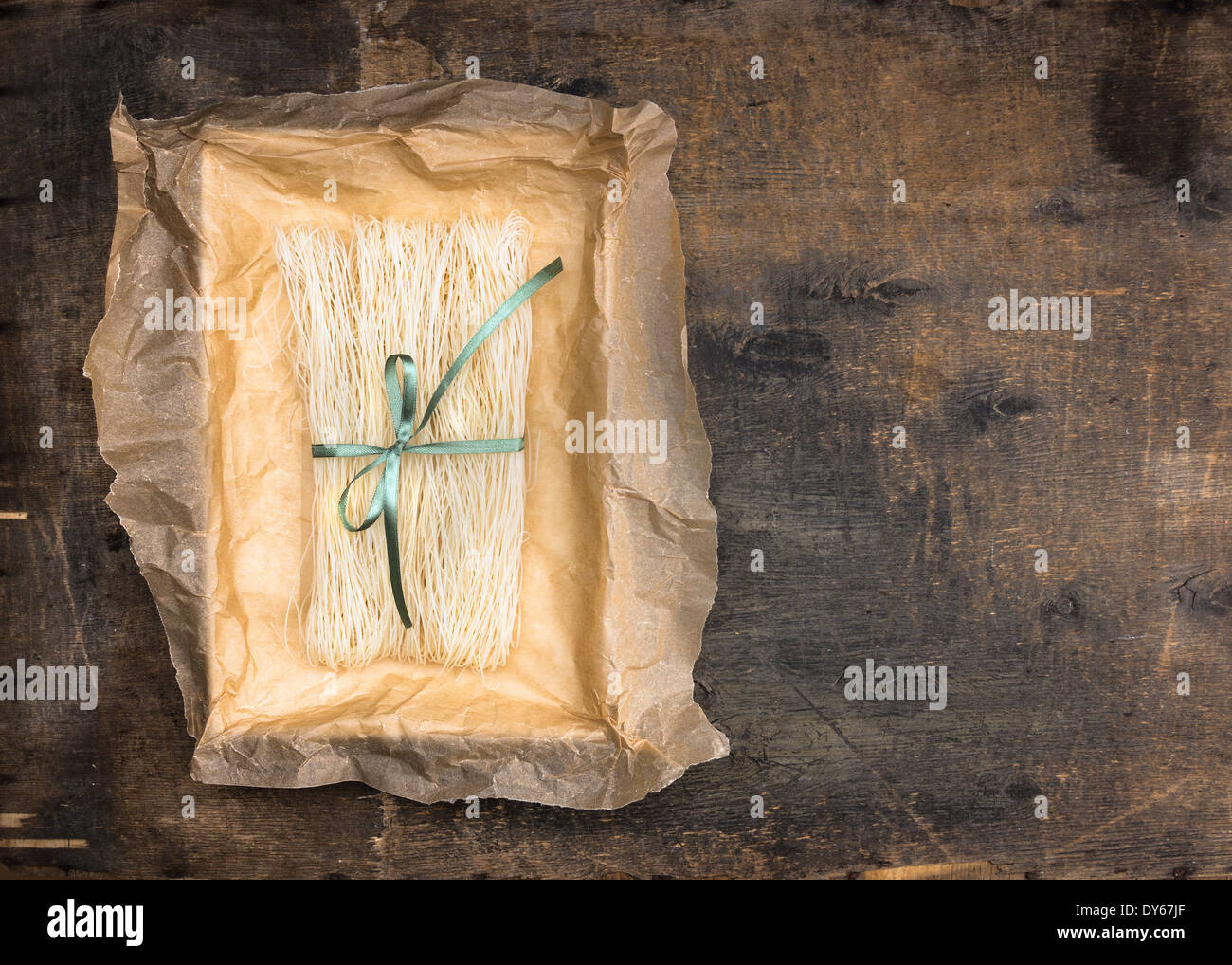 Il cinese riso tagliatelle in carta sgualcita confezione con nastro verde su un vecchio tavolo in legno Foto Stock