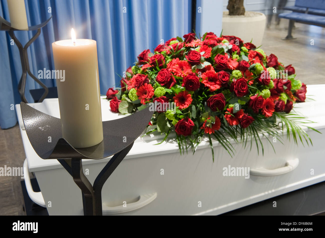 Una bara con un omaggio floreale in un obitorio e una candela che brucia nella parte anteriore Foto Stock