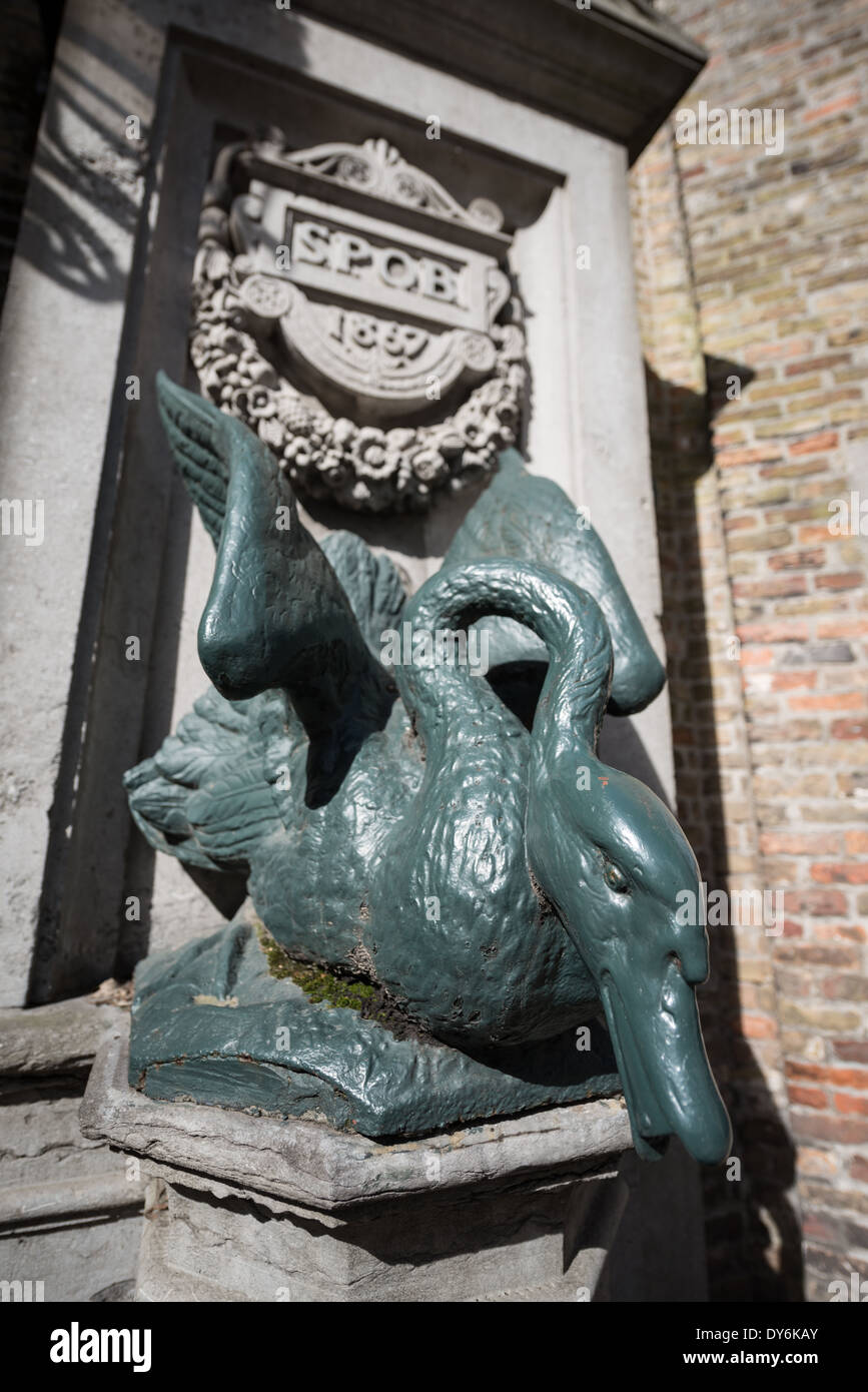 BRUGES, Belgio - Una statua di cigno forma una fontana di acqua potabile nel centro storico di Bruges, Belgio. L'architettura medievale e i sereni canali modellano il paesaggio urbano di Bruges, spesso chiamato "la Venezia del Nord". Essendo una città patrimonio dell'umanità dell'UNESCO, Bruges offre ai visitatori un viaggio nel passato dell'Europa, con i suoi edifici ben conservati e le strade acciottolate che riflettono la ricca storia della città. Foto Stock