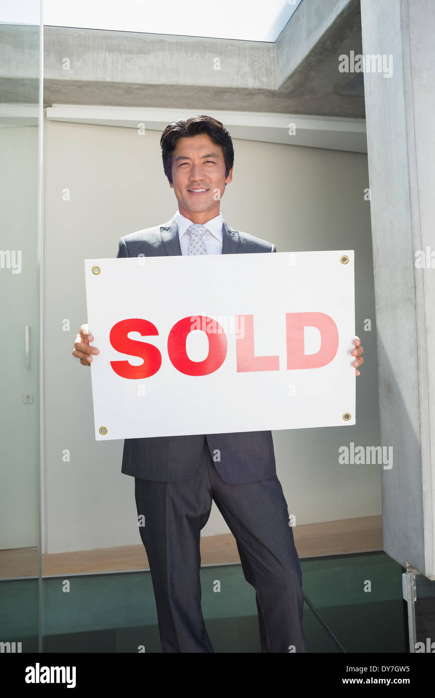 Fiducioso agente immobiliare in piedi davanti alla porta di casa che mostra venduti segno Foto Stock