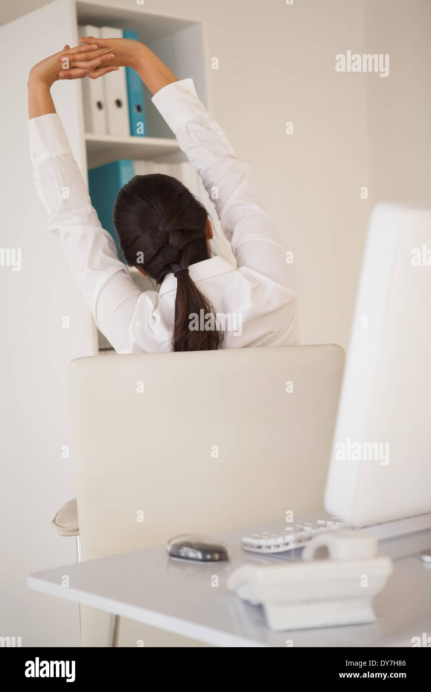 Casual imprenditrice stretching alla sua scrivania Foto Stock