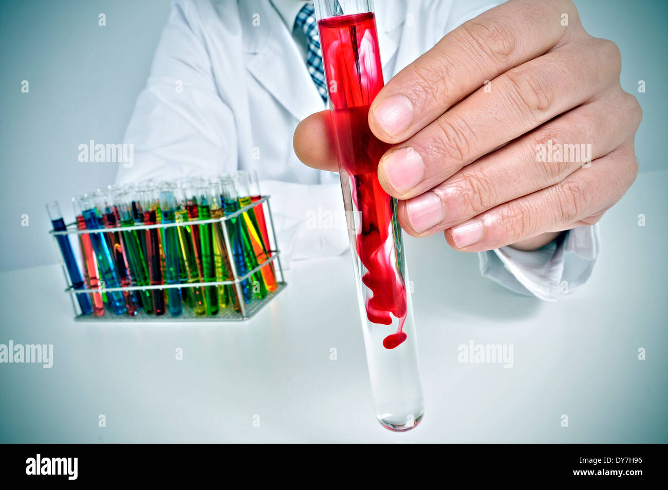 Uomo in camice bianco seduto su una scrivania con provette con liquidi di colori differenti in un laboratorio Foto Stock