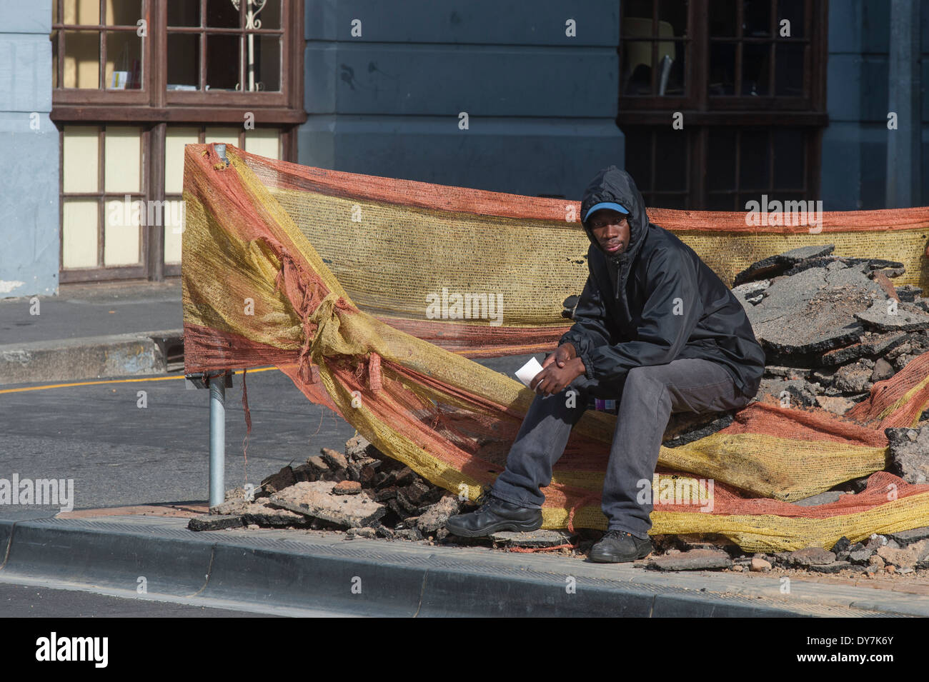 Senzatetto uomo seduto su alcuni detriti di costruzione sito, Cape Town, Sud Africa Foto Stock