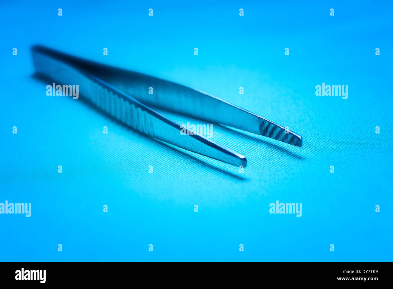 Strumenti chirurgici - usurati, graffiati una pinza chirurgica su tende in blu luce clinica con profondità di campo ridotta. Foto Stock