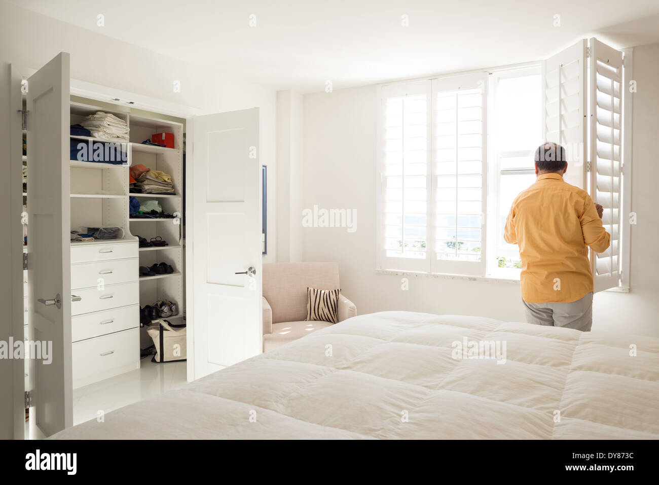 L'uomo apertura persiane in tutto bianco soleggiate, luminose, mostrare la camera da letto padronale, STATI UNITI D'AMERICA Foto Stock