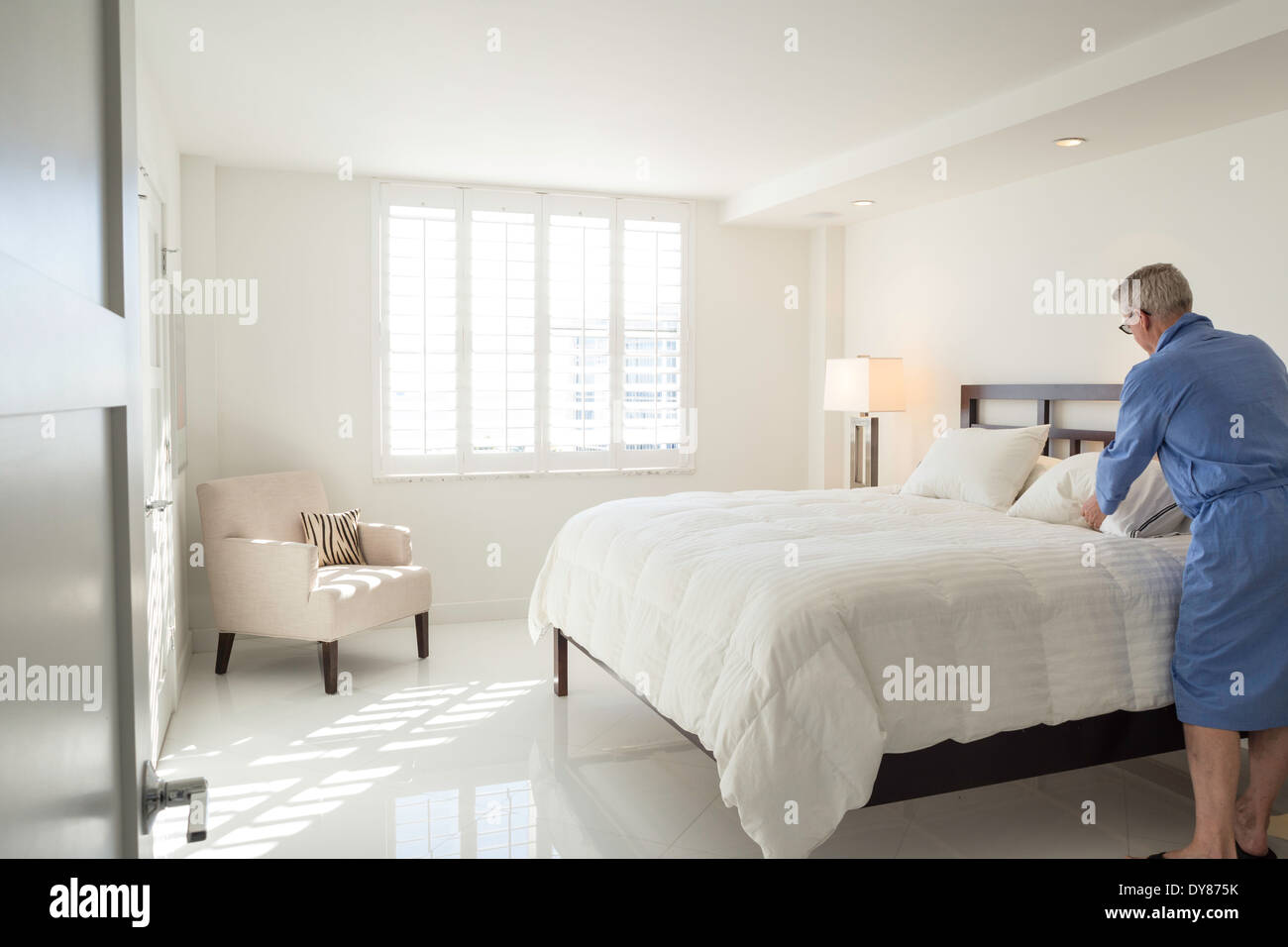 Uomo maturo in accappatoio rendendo letto, lussuoso condominio, STATI UNITI D'AMERICA Foto Stock