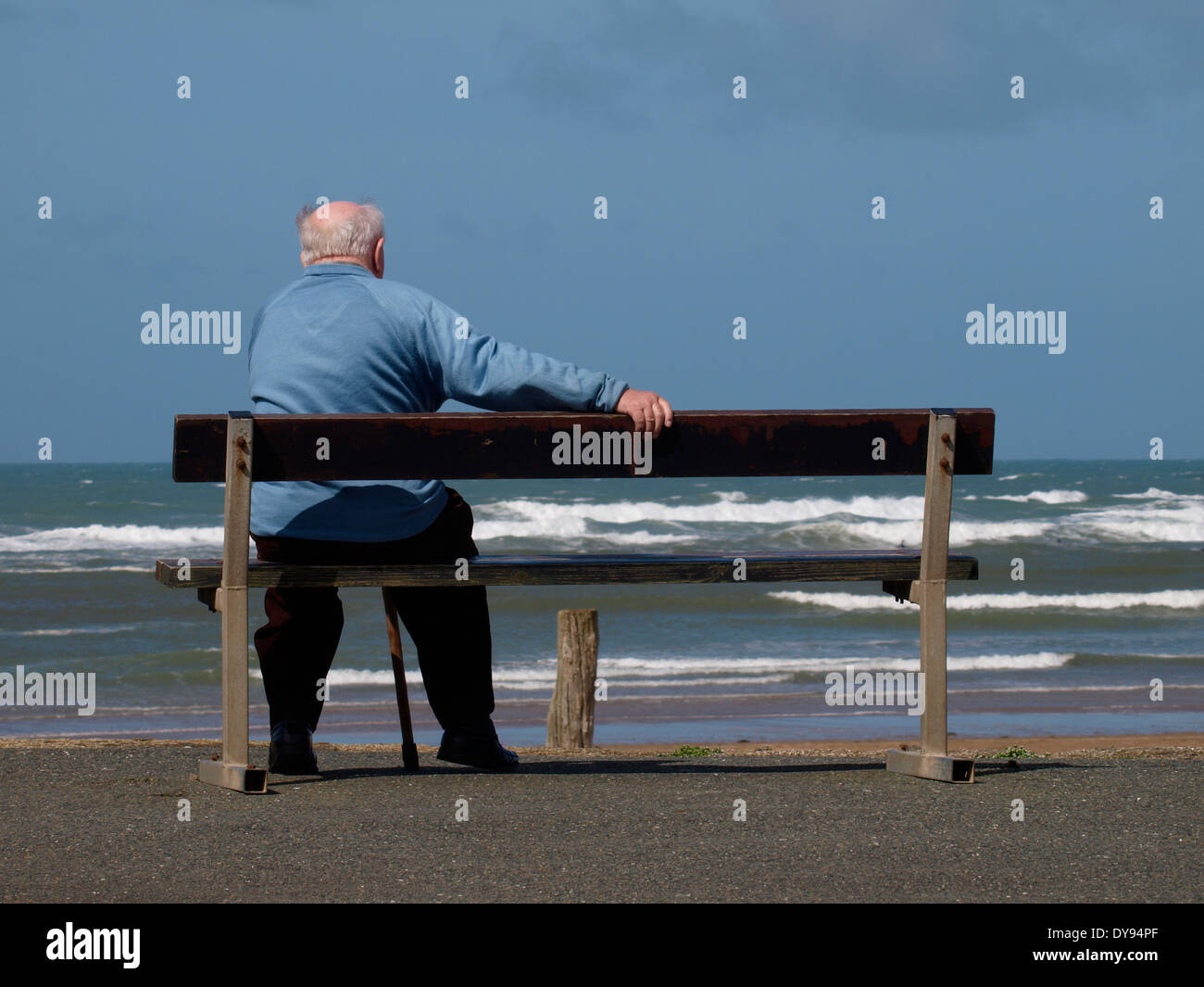 Il vecchio uomo seduto su una panchina pubblica che si affaccia sul mare, Bude, Cornwall, Regno Unito Foto Stock