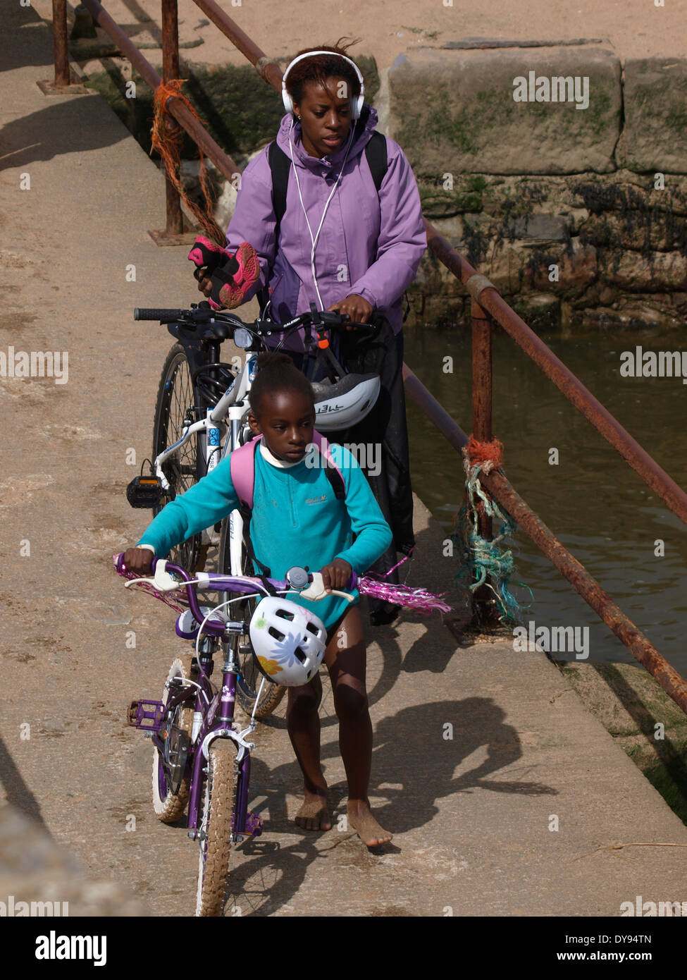 Black British madre e figlia spingendo le biciclette oltre il ponte pedonale, Bude, Cornwall, Regno Unito Foto Stock