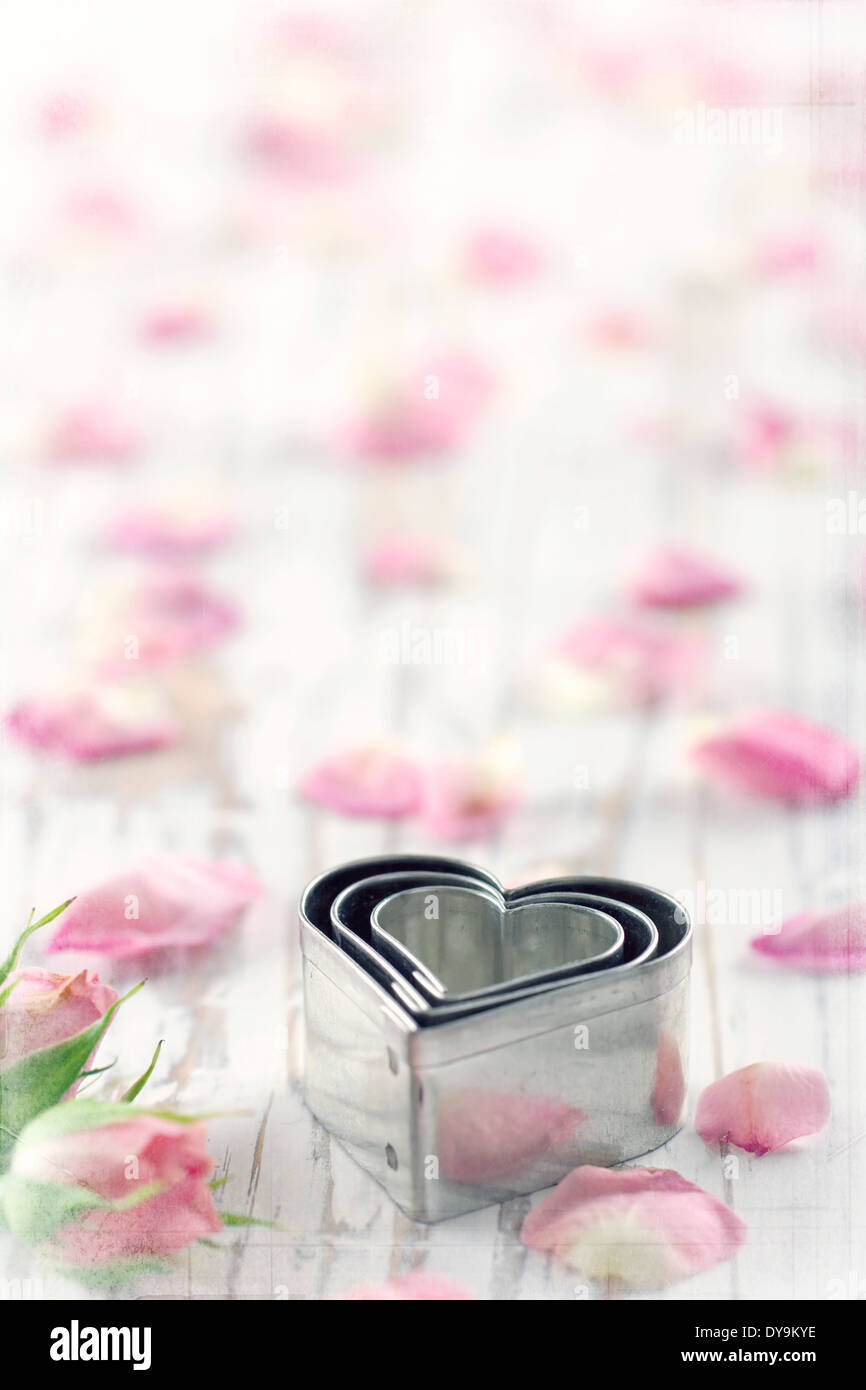 A forma di cuore ad cookie cutters su un vecchio bianco vintage sfondo in legno di rosa con petali di fiori Foto Stock