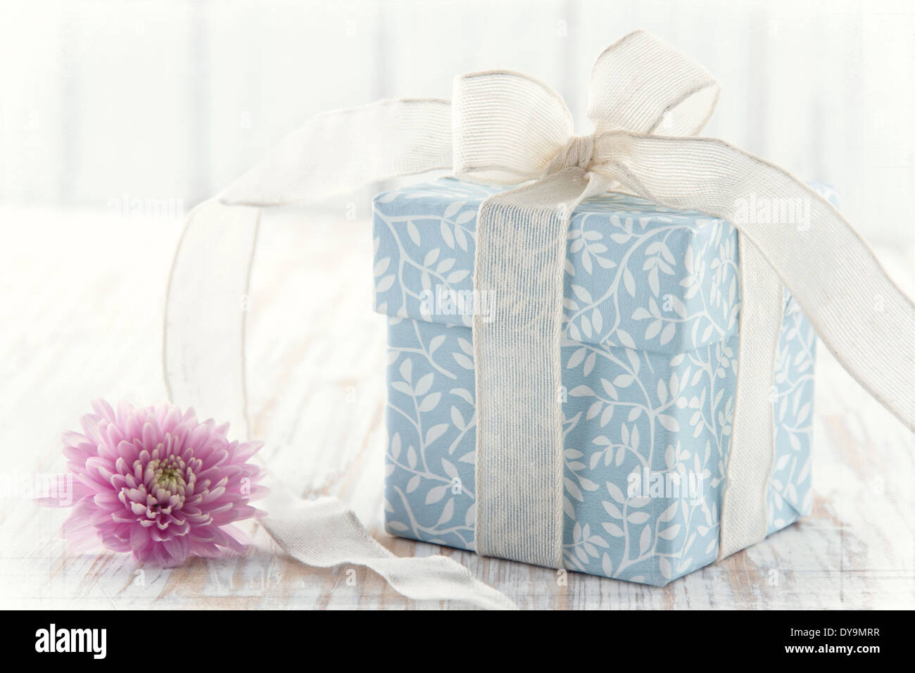 Luce con motivi floreali blu scatola regalo legato con nastro bianco e fiore rosa su rustiche in legno e di sfondo texured editing vintage Foto Stock