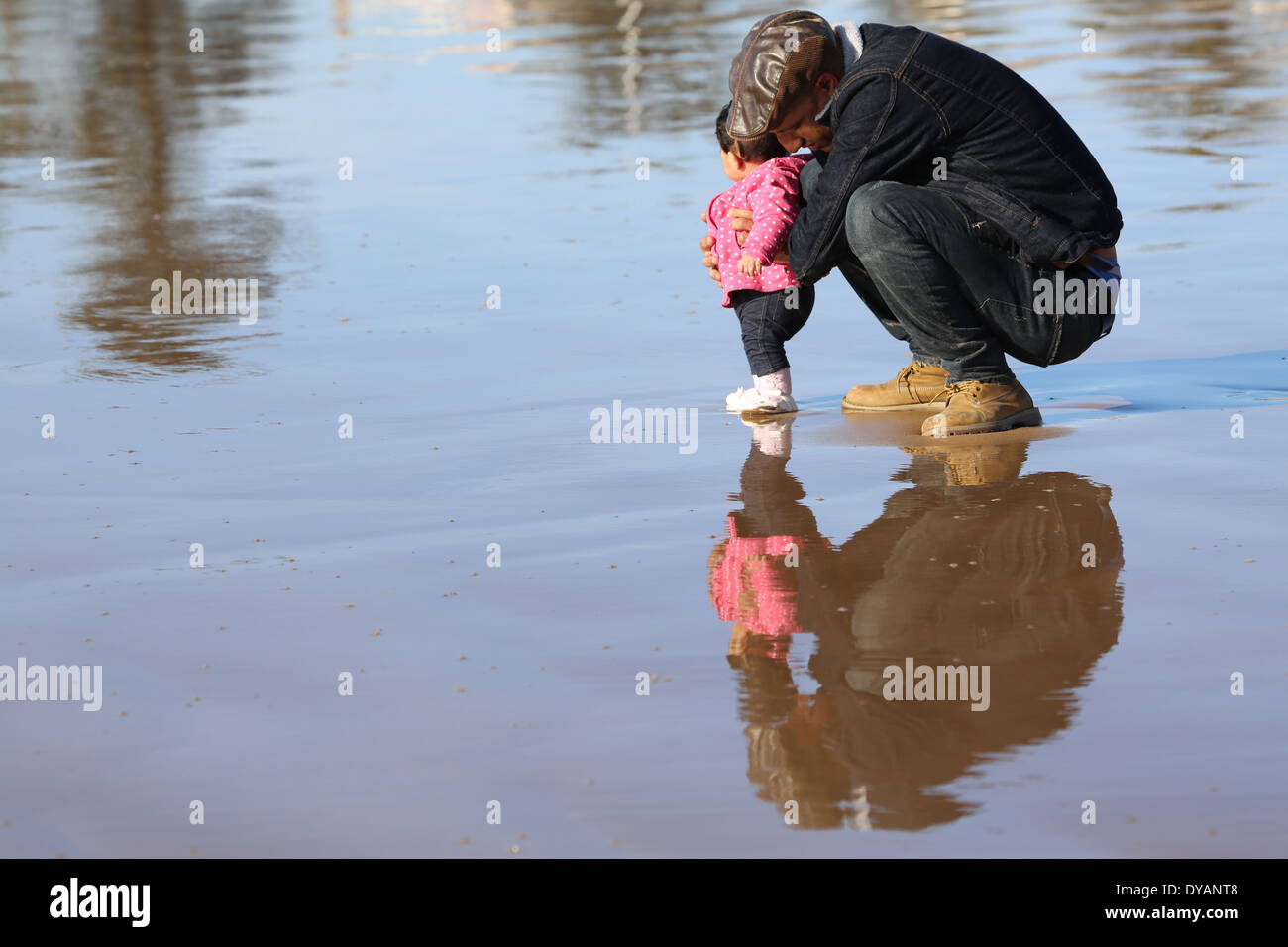 Padre coying oltre il toddler figlia su un wet spiaggia sabbiosa a Essaouira, Marocco, non vedendo un'onda in arrivo fino a molto ultimo minu Foto Stock