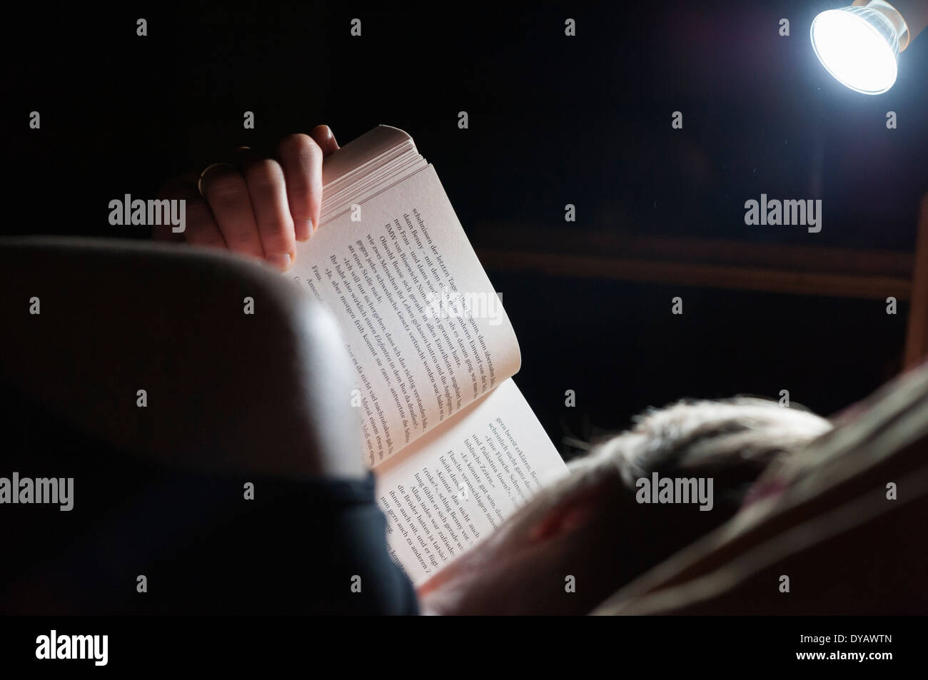 Una donna è disteso nel suo letto e la lettura di un libro come lezione prima di addormentarsi. Foto Stock