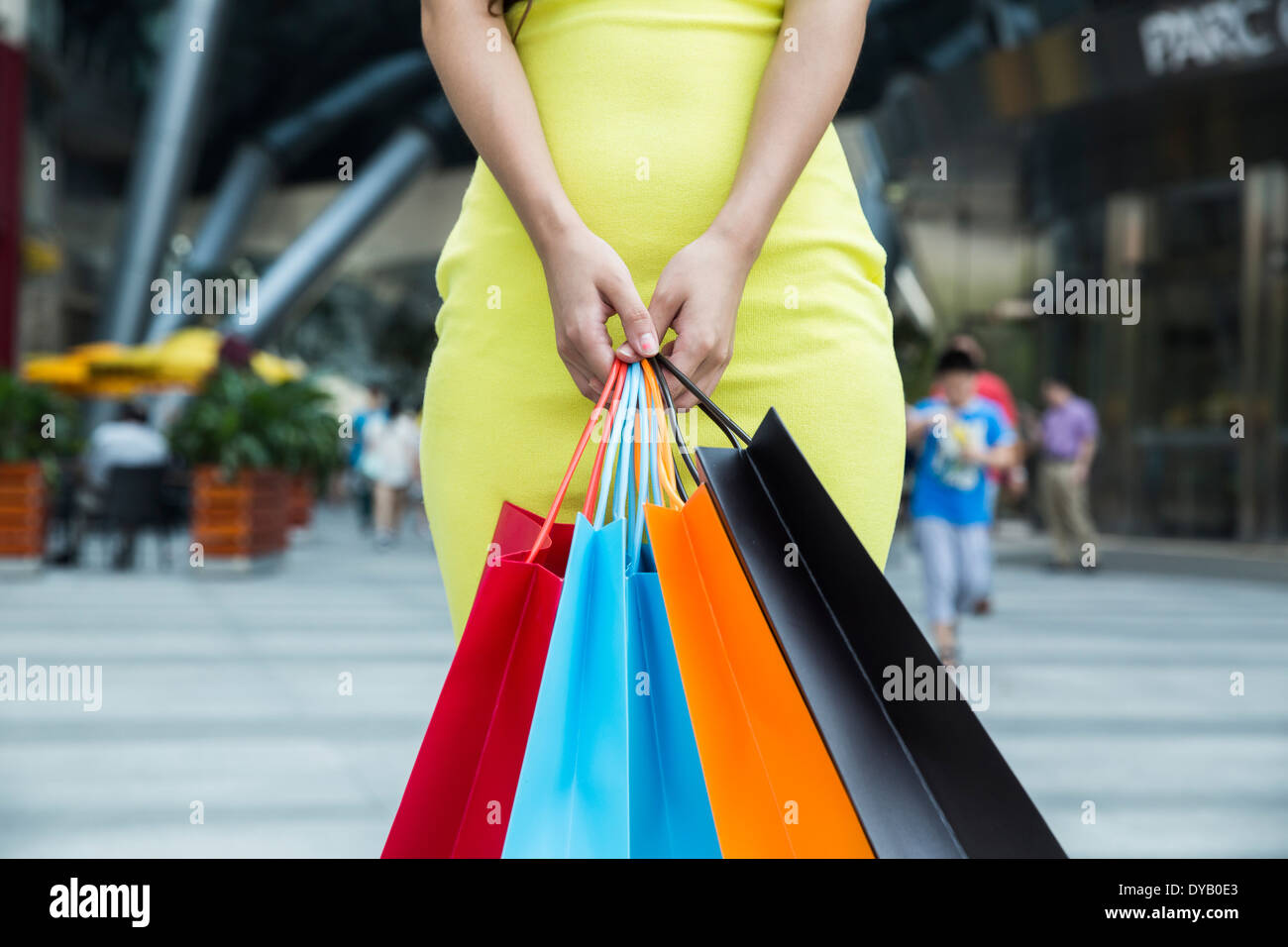 Donna con borse per lo shopping nel centro commerciale, che indossa un mantello giallo. Foto Stock