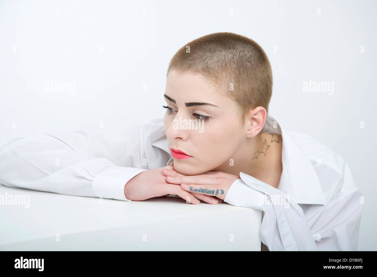 Donna con una testa rasata appoggiata contro una casella bianca. Foto Stock