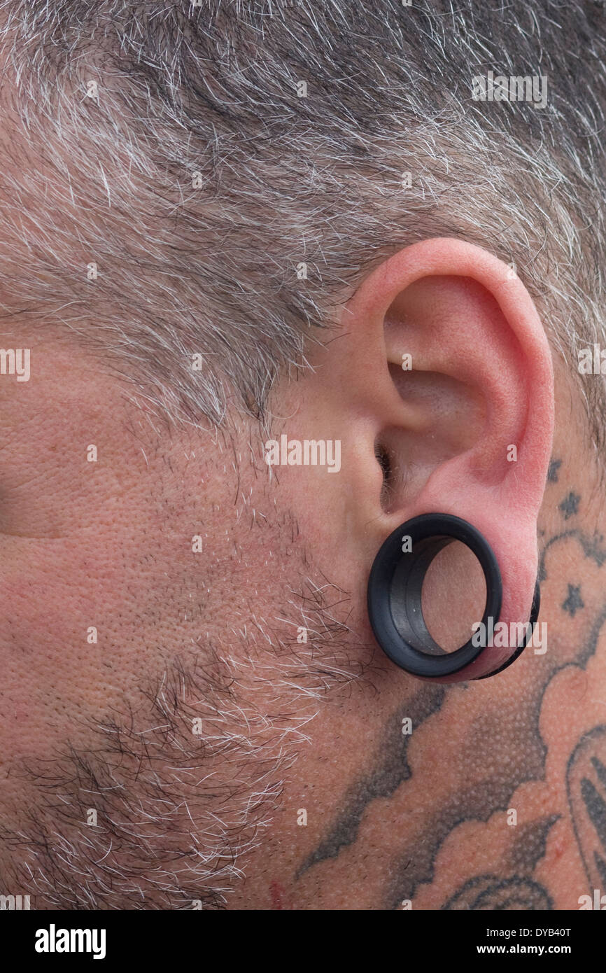Vista laterale di un uomo con una stirata lobo orecchio e tatuaggi Foto Stock