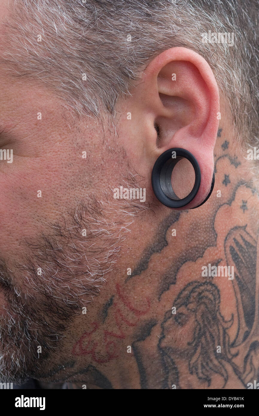 Vista laterale di un uomo con una stirata lobo orecchio e tatuaggi Foto Stock