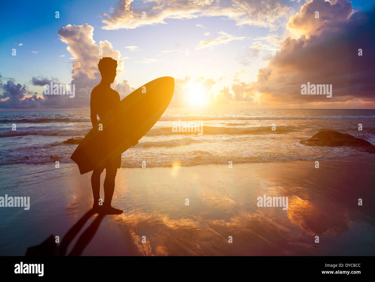 Surfer uomo in piedi sulla spiaggia e in possesso di una tavola da surf Foto Stock