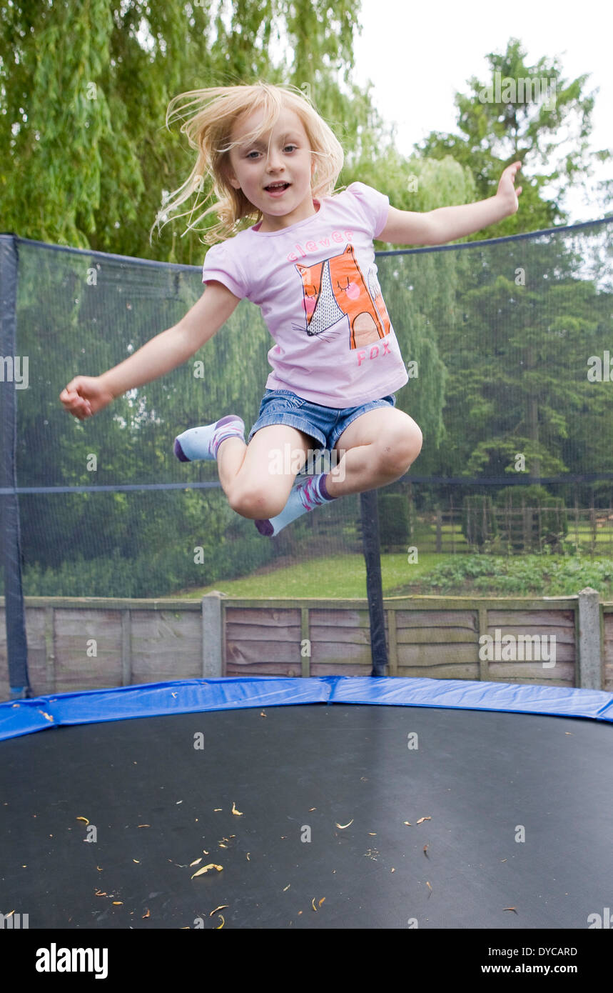 Ragazza di età compresa tra i 5- 6 sul trampolino che rimbalza nel suo giardino sul retro Foto Stock