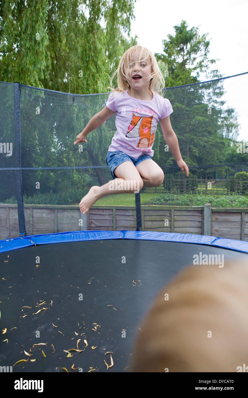Ragazza di età compresa tra i 5- 6 sul trampolino che rimbalza nel suo giardino sul retro Foto Stock