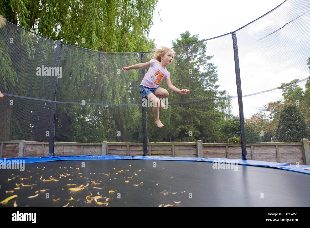 Ragazza di età compresa tra i 5- 6 sul trampolino che rimbalza nel suo giardino sul retro Foto Stock