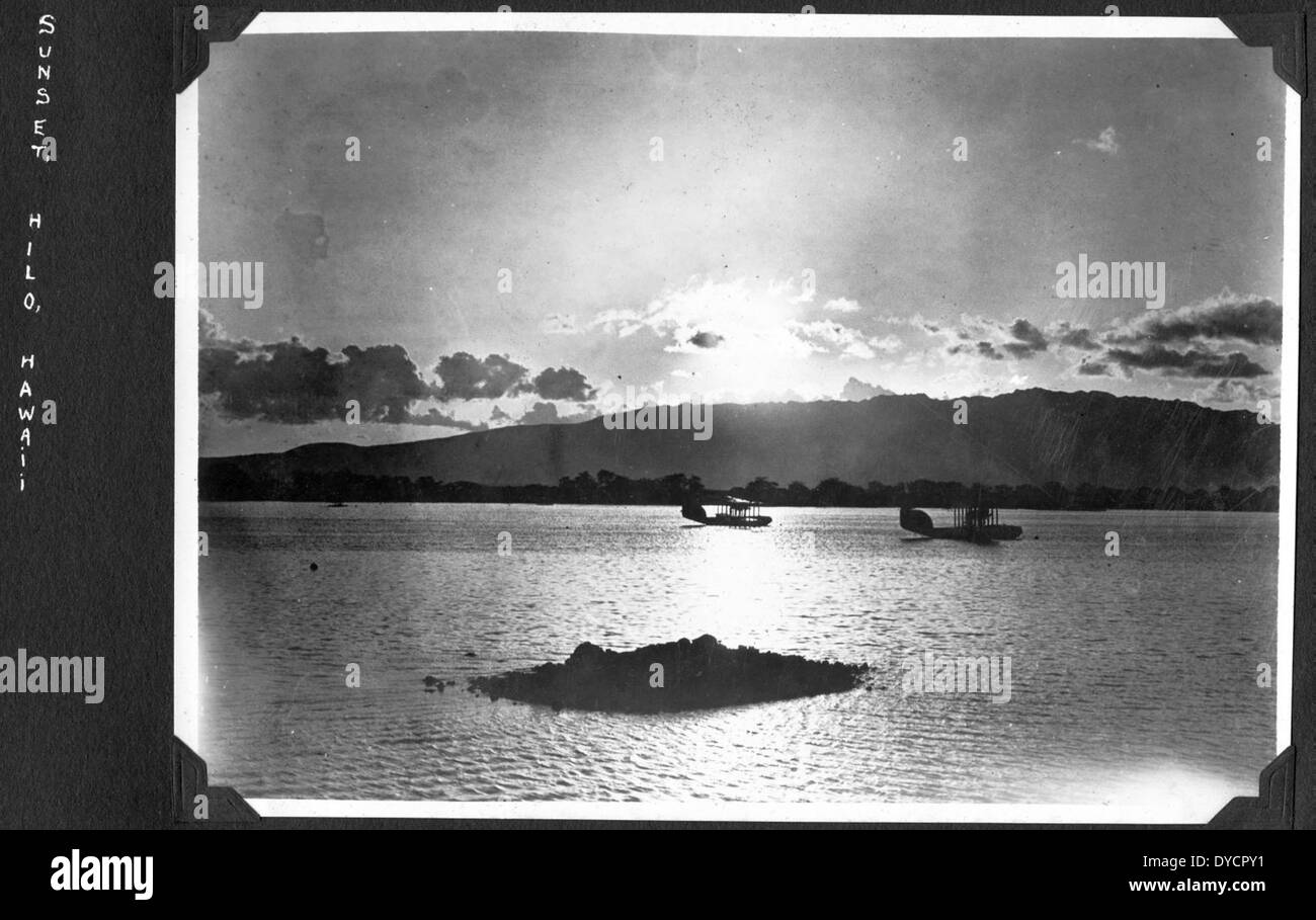 Questa immagine cattura un tramonto su Hilo con la USS Langley (AV-3) in lontananza. La USS Langley fu la prima portaerei americana, inizialmente commissionata come tender per idrovolanti nel 1922, giocando un ruolo significativo nell'aviazione navale durante il suo periodo di servizio. Foto Stock