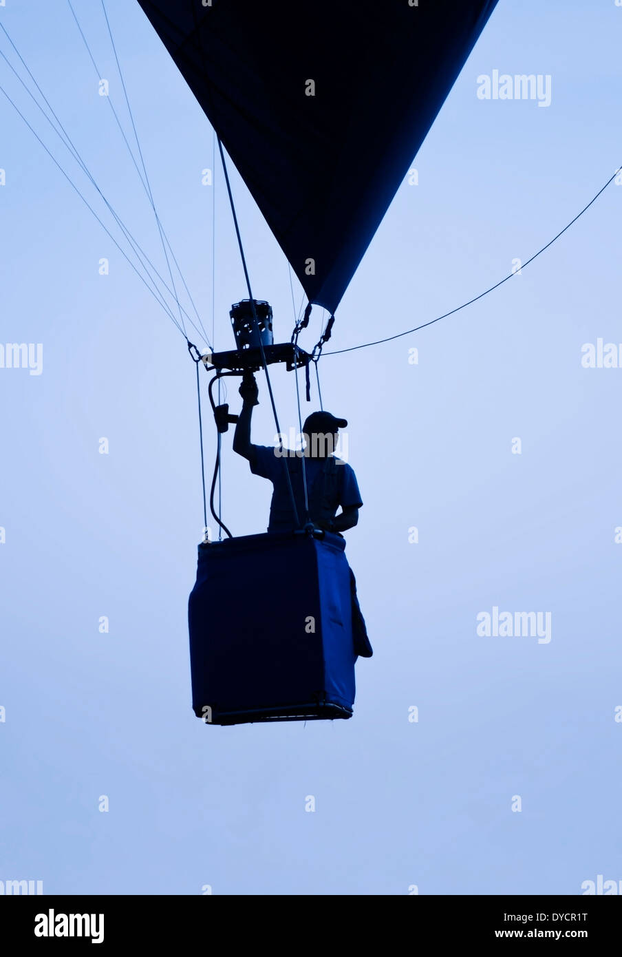 Un uomo il pilotaggio di una sola persona mongolfiera rising profilarsi davanti un nebuloso cielo blu Foto Stock