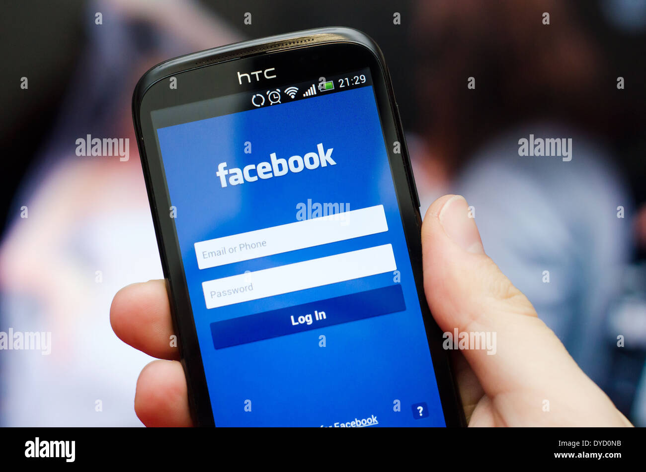 Mano azienda smartphone con il social network Facebook mobile app con interfaccia in inglese Foto Stock