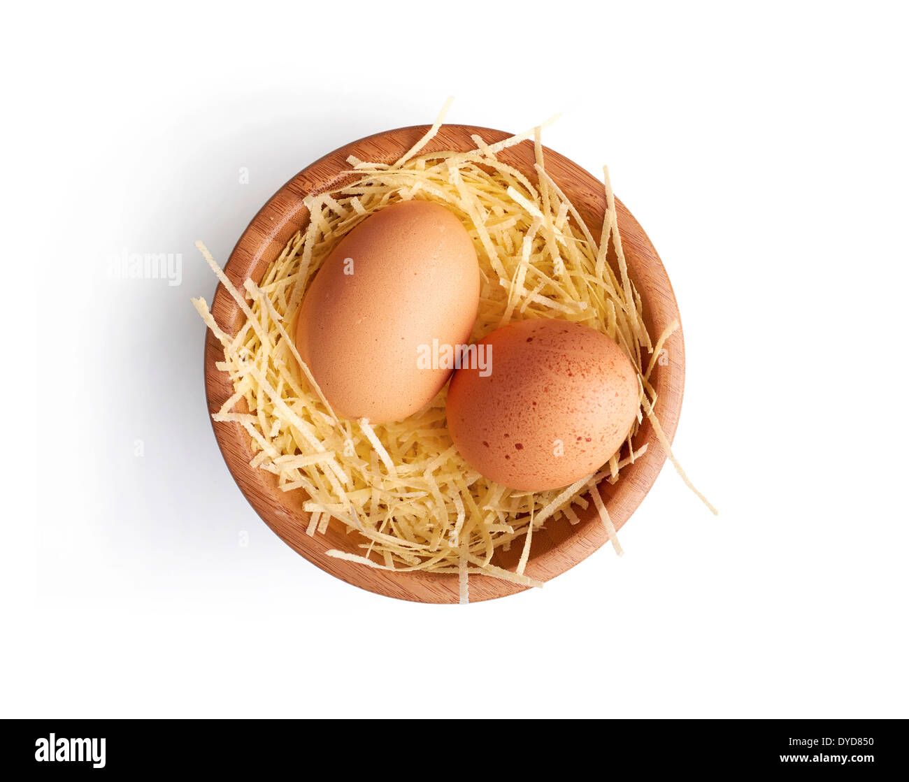 Due fresche uova di galline su un po di paglia in una ciotola di legno su uno sfondo bianco. Foto Stock